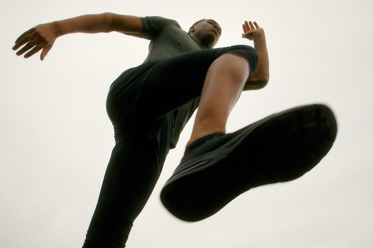 Low-angle view of a person in black athletic wear running or leaping, emphasizing the sole of their shoe and dynamic motion.
