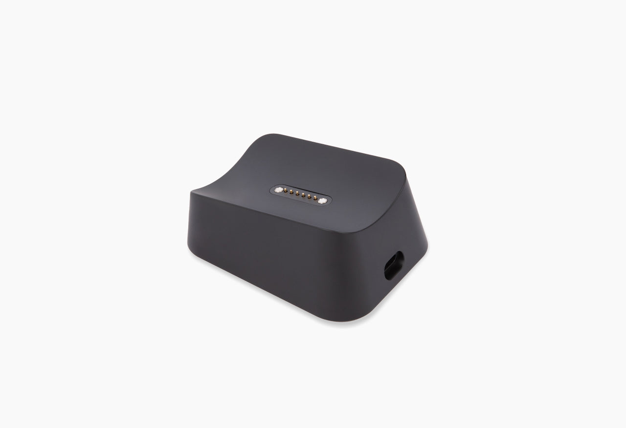 Matte black charging dock/cradle with exposed gold multi-pin connector on top and a side cable port