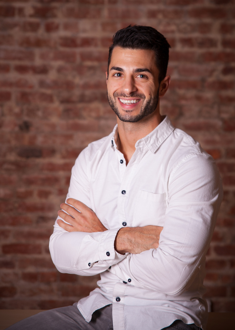 Dr Daniel Giordano with crossed arms in a white shirt against a brick wall